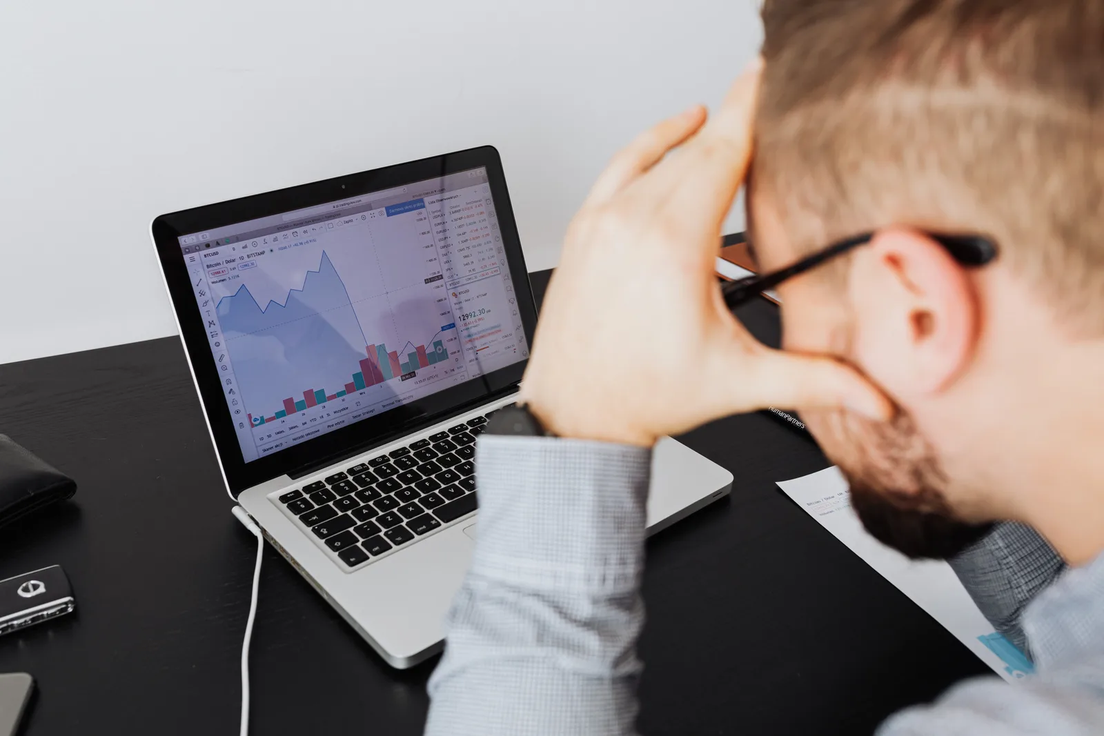 Over the shoulder view of a man analyzing financial data on a laptop screen.