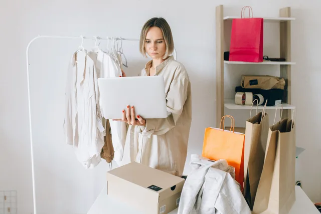 Woman using laptop for online shopping with clothes and bags around her, indoors. Ecommerce SEO costs: retainers and worked examples